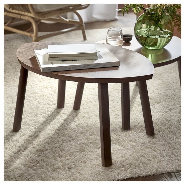 Two round coffee tables on a white rug with books, glass, and green plants.