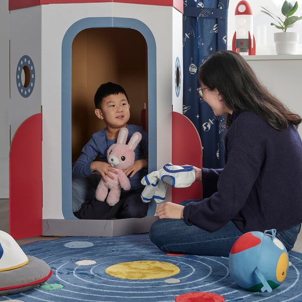 Person & child play in cardboard space station, toys in hand.