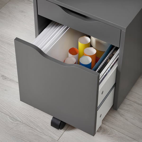 Grey ALEX drawer unit with open bottom drawer showing coloured cylindrical items and a binder.