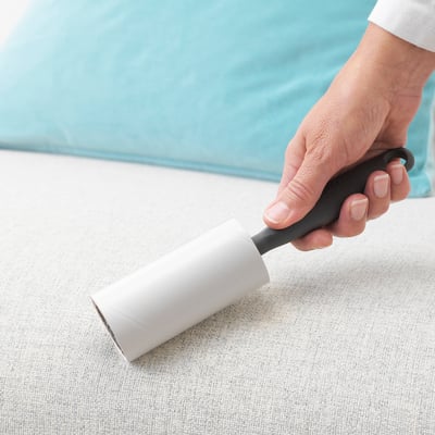 Hand holds BÄSTIS lint roller on fabric.