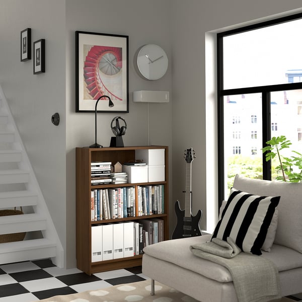 Cosy corner with BILLY bookcase, books, media, striped pillow couch, leaning guitar, clock, art, speaker, chequered floor staircase.
