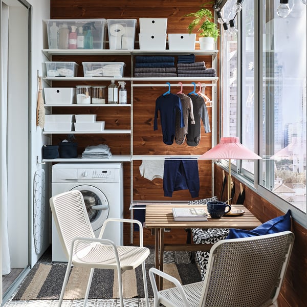 Organised laundry room with BOAXEL storage system, white, steel, shelves, hangers, washing machine, chairs, and plant.
