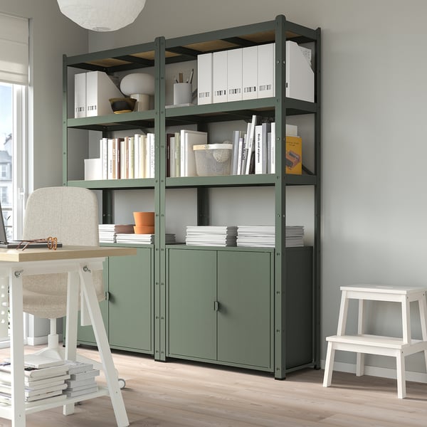 BROR green storage: shelves with books, boxes, & decor. White desk, chair, & stool at sides.