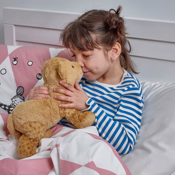 Girl in striped pyjamas hugs soft, huggable lion toy in bed.