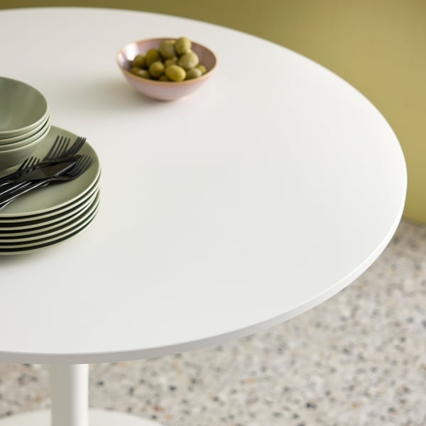 Small round white DOCKSTA table with green plates and forks, a bowl of olives, and a patterned floor.