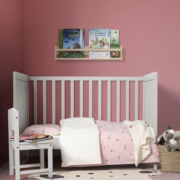 Childs nursery with pink walls, white DRÖMSLOTT rug, white crib, and wooden book shelf.