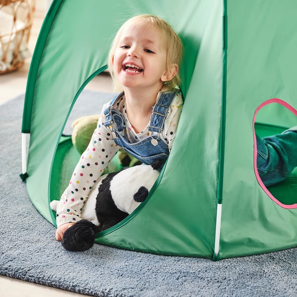 Little girl laughing in green tent, hugging stuffed panda. Fun and cosy play area.