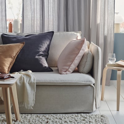 A cosy grey sofa with multiple cushions and blankets. Soft textiles, varied textures, and warm decor create a welcoming living space.