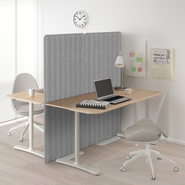 Modern office setup with noise-reducing screen, laptops, coffee mugs, and wooden desk.