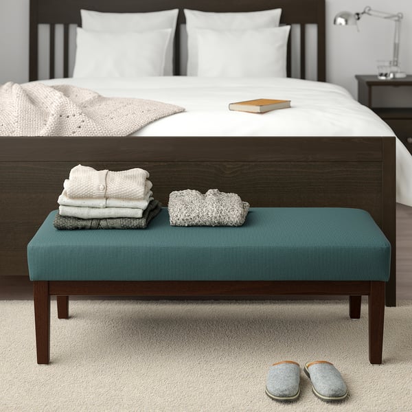 Blue EKENÄSET bench with towels and decor by bed, slippers in front.