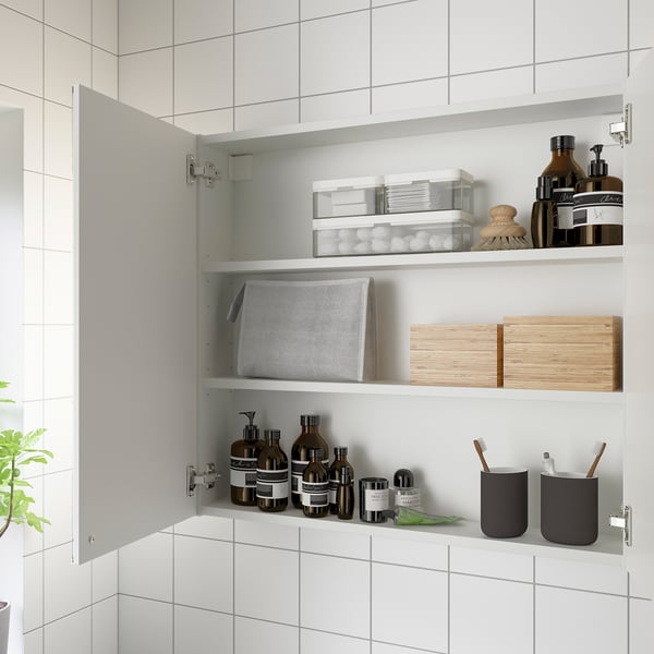 Open bathroom cabinet with mirror doors displaying shelves, holding various items like toiletries, containers, and wooden boxes.