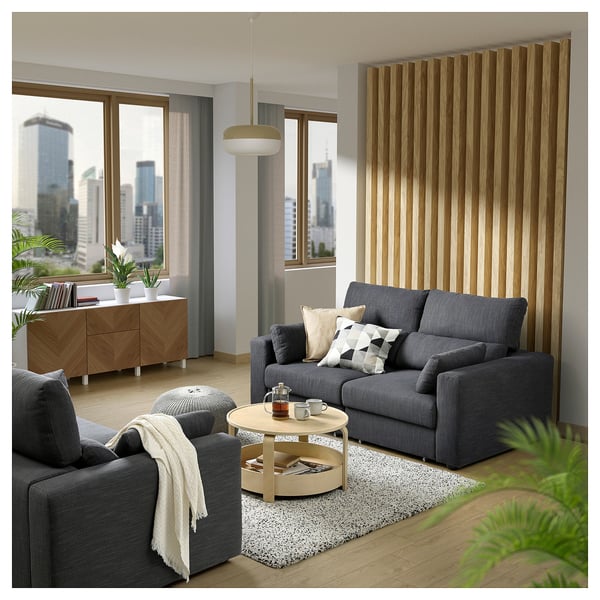Modern living room with grey ESKILSTUNA sofa, wool rug, wooden coffee table, and city view.