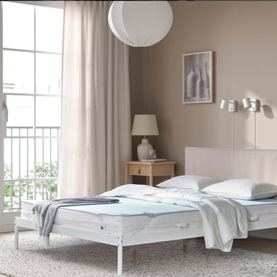 HÅRGINST mattress protector on bed, fitting neatly under window in serene bedroom.