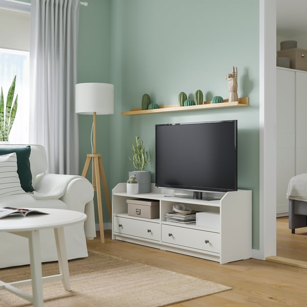 Modern living room with white tv stand, flat screen, cacti decorations, potted plants, and a cosy seating area by the window.