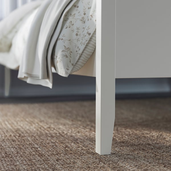 Bed frame leg in white, part of the IDANÄS set, positioned on a woven floor mat.