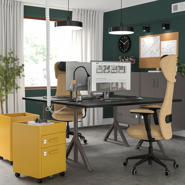 Modern office with IDÅSEN desks, yellow cabinets, ergonomic chairs, monitors, and hanging lamps.
