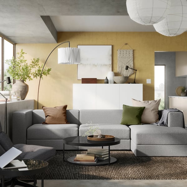 Modern living room with grey JÄTTEBO modular sofa, mustard walls, white art, and hanging lights.