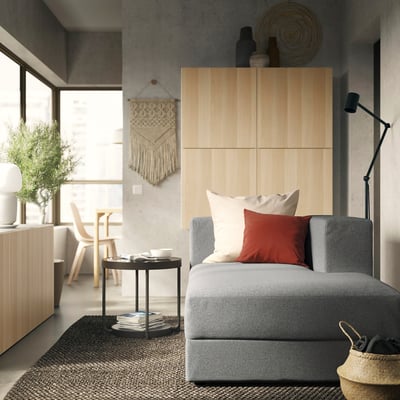 Cosy living room with JÄTTEBO grey sofa, red pillows, wooden decor, floor lamp, and plants.
