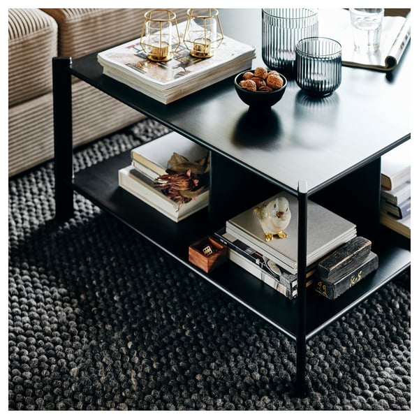 Black 3-tier JÄTTESTA shelf, displaying books, decor, and bowl with snacks and candles. Sleek metal legs, bamboo shelves. Modern, functional design.