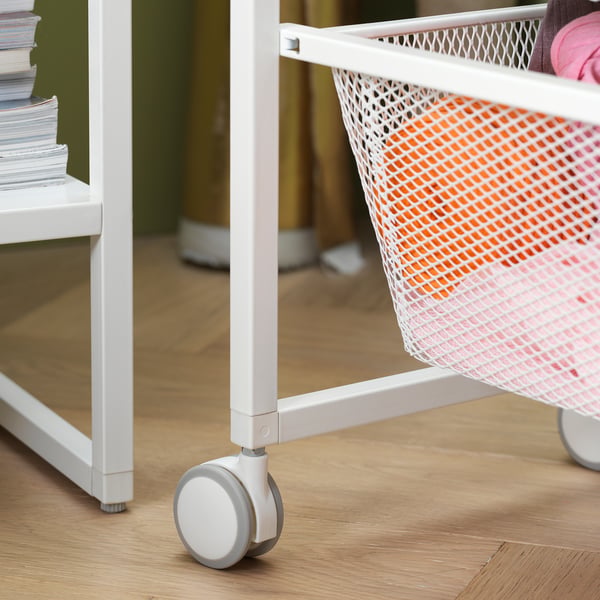 White JONAXEL storage trolley with wheels, mesh basket holding pink items, wooden floor.