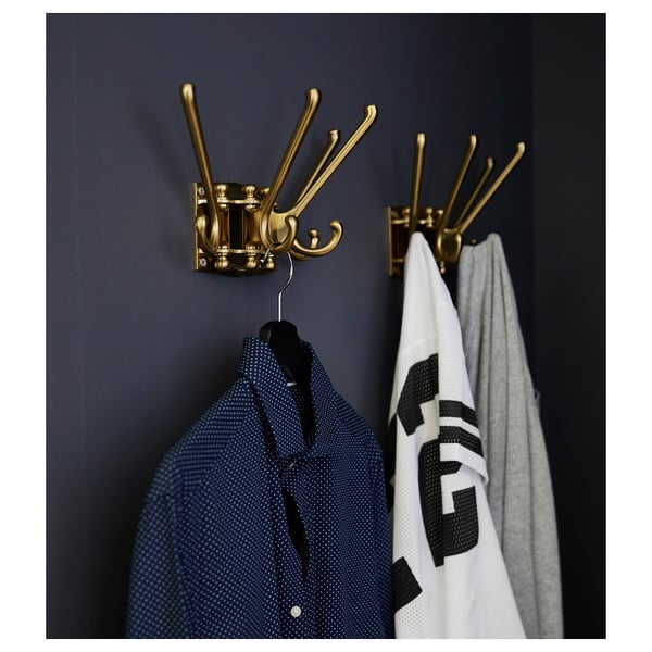 Three golden hooks hang on a dark wall. A blue shirt and a white towel dangle from them.