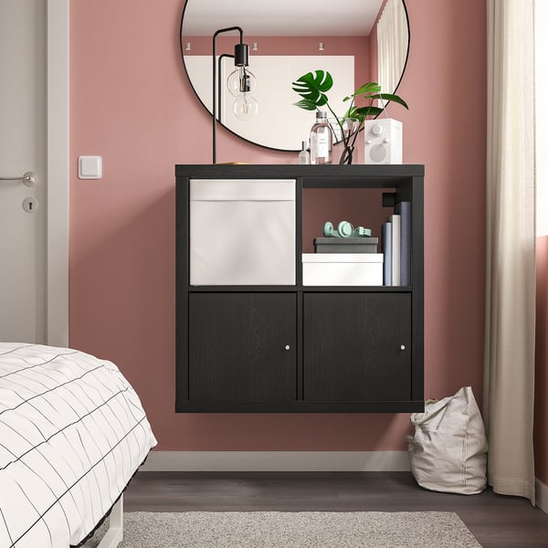 Modern bedroom with black KALLAX storage, books, decor, plant, mirror, and plaid bed.