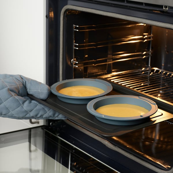 Person placing baking moulds with batter into an oven, using oven mitts.