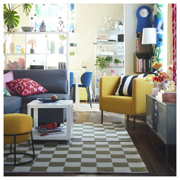 Bright living room with grey sofa, yellow armchairs, chequered rug, white coffee table, colourful decor, and large window.