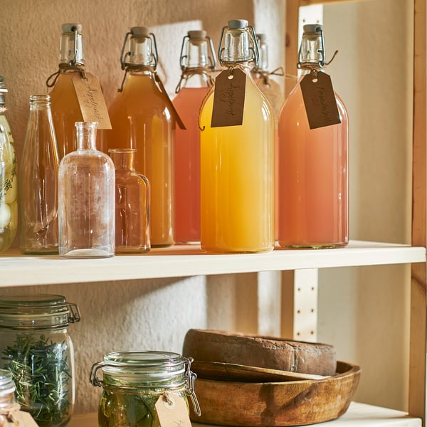 Shelf with glass jars, some filled with colourful liquids, and a wooden bowl holding bread.