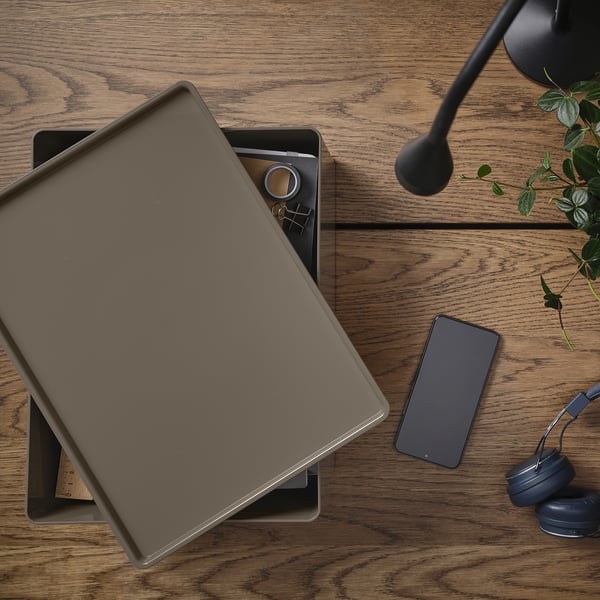 Wooden desk with closed laptop, smartphone, headphones, and small plant. Ideal for remote work setup.