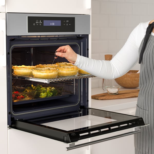 A person in an apron uses a thermometer to check baked goods in an open self-cleaning, convection oven with touch controls.