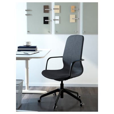 Modern office chair with height-adjustable seat, armrests, and lumbar support positioned near a white desk with a stack of books and a coffee cup.