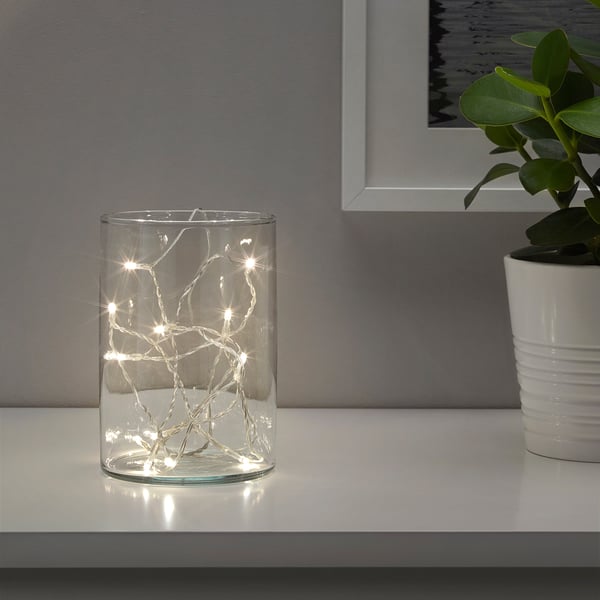 Clear vase with warm led lights, plant beside, cosy decor.