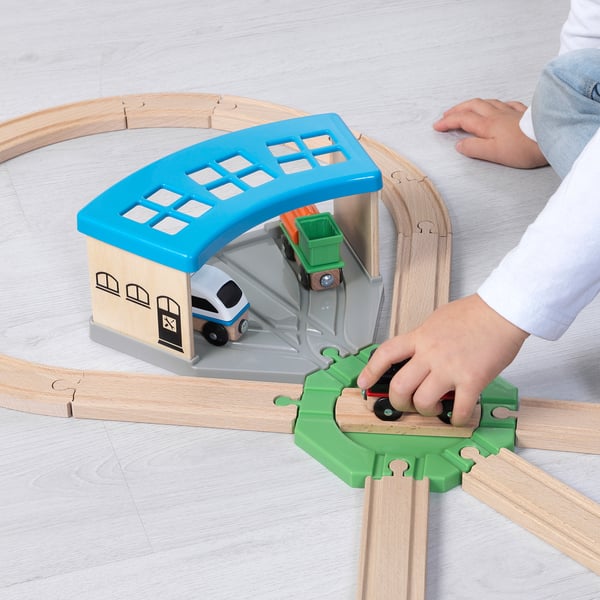 Child playing with LILLABO train set, using a green turntable to change train direction on a wooden track.
