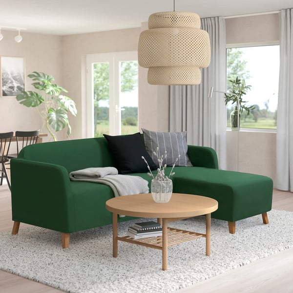 Green LINANÄS sofa with black and grey pillows, wooden round coffee table, magazines, and a large natural pendant light above.