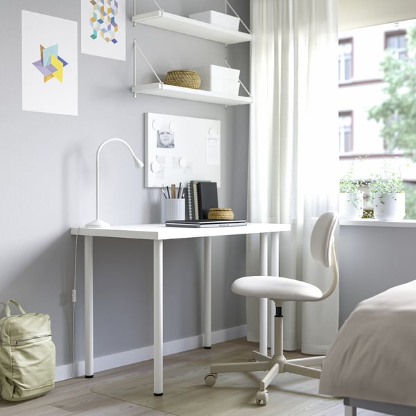 Minimalist home office with white desk, shelves, lamp, notebooks, and chair. Bright space with large window and artwork.