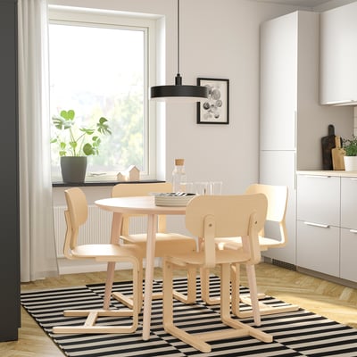 A modern dining setup with a wooden table, chairs, black pendant light, and a plant by the window.