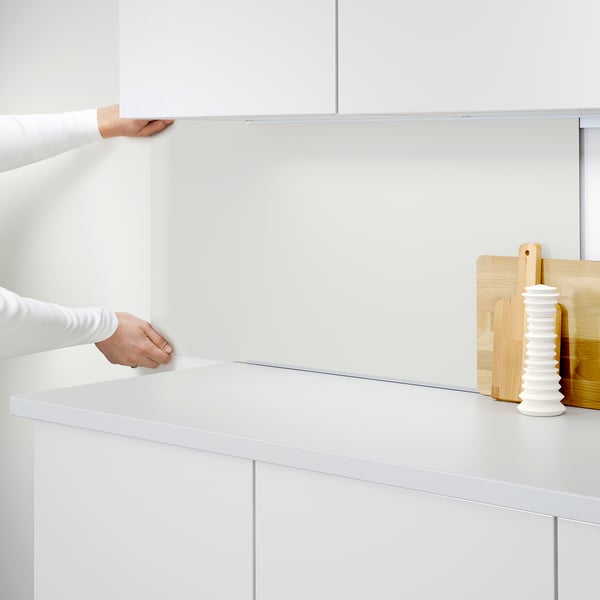 A person instals a LYSEKIL wall panel, protecting kitchen walls from splashes and grease, shown in white.
