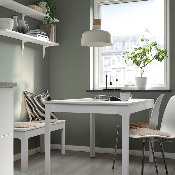 Cosy workspace with white table, two cushioned chairs, green walls, lamp & plant.