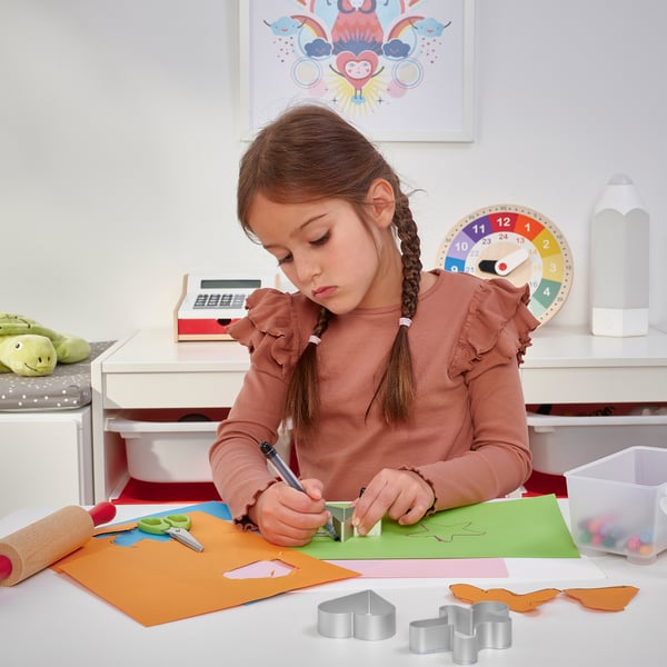 A young girl is crafting, using colourful paper and shapes, focusing on the person work at a desk.