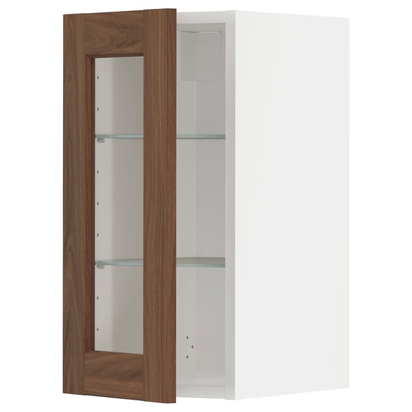 A METOD wall cabinet with a white frame and a walnut-finished glass door featuring adjustable shelves.