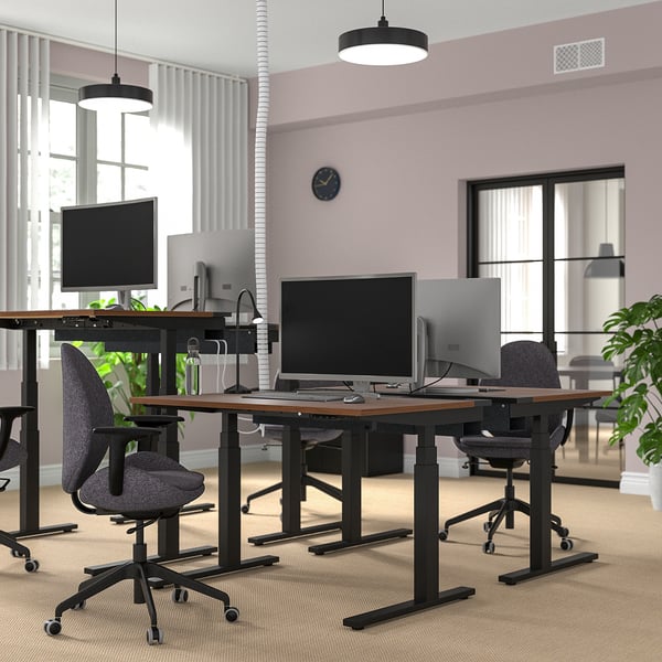 Modern office space with MITTZON sit/stand desks. Dark wooden tops & black metal frames. Computers, chairs, and plants. Bright, open setting.
