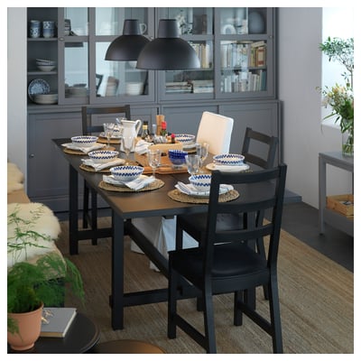 Modern kitchen with black dining set, grey cabinet, blue dishware, hanging lamps, and potted plants.