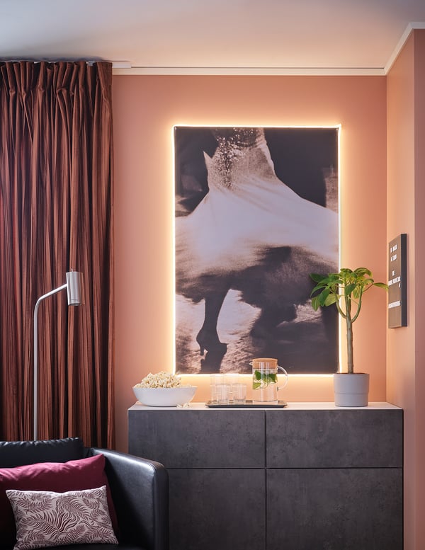 Modern living room with light strips; large abstract photo, dark furniture, and red curtains.