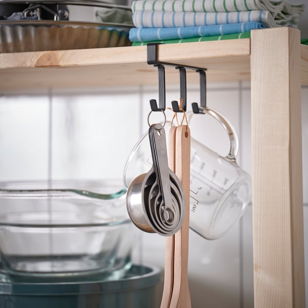 Kitchen hooks on shelf holding measuring cups and spoon.