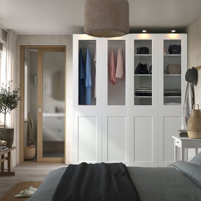 Bedroom with white PAX wardrobe, glass doors, grey bed, wooden mirror, wicker lamp, wall decor.