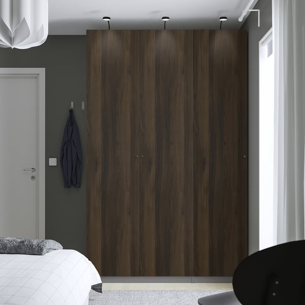 Modern bedroom with large dark wood PAX wardrobe, blue garment, and minimalist decor.