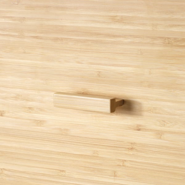 A close-up view of a sleek, light-colored wooden drawer handle on a smooth, natural-finished wooden surface.