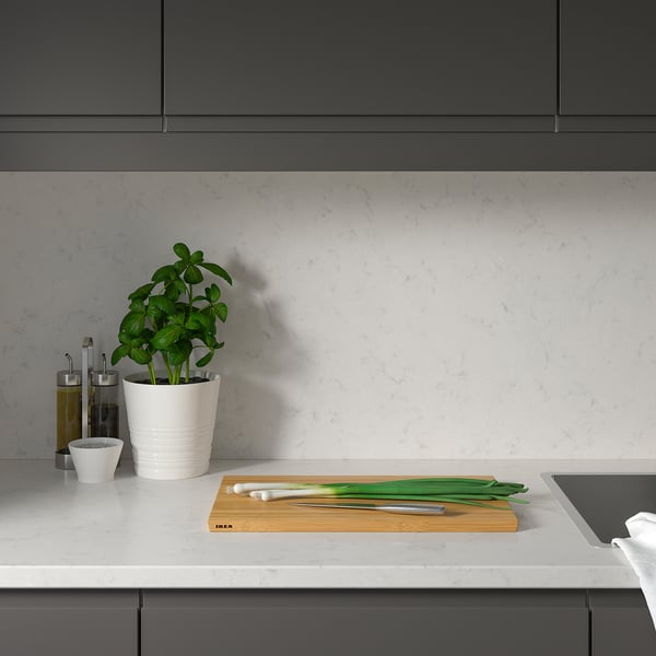 Modern kitchen with white quartz countertop, plant, onions, knife; grey cabinets.