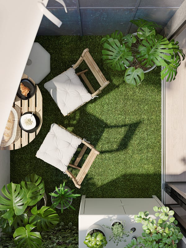 Small green balcony with white foldable chairs, round coffee table, plants, and artificial grass floor.